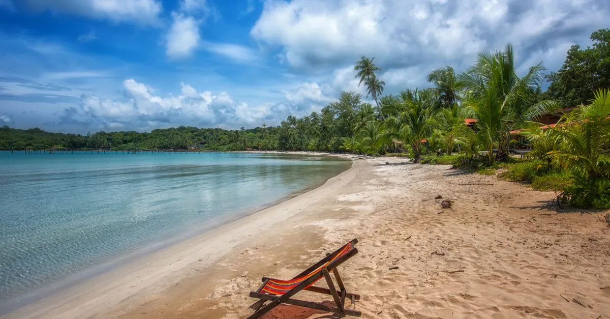 Tranquila escena de playa tropical con palmeras y una tumbona solitaria bajo un cielo vibrante.